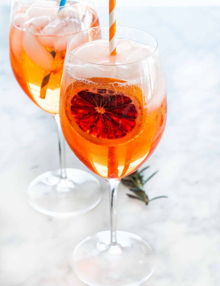 two wine glasses full of aperol spritz garnished with a slice of blood orange and straw