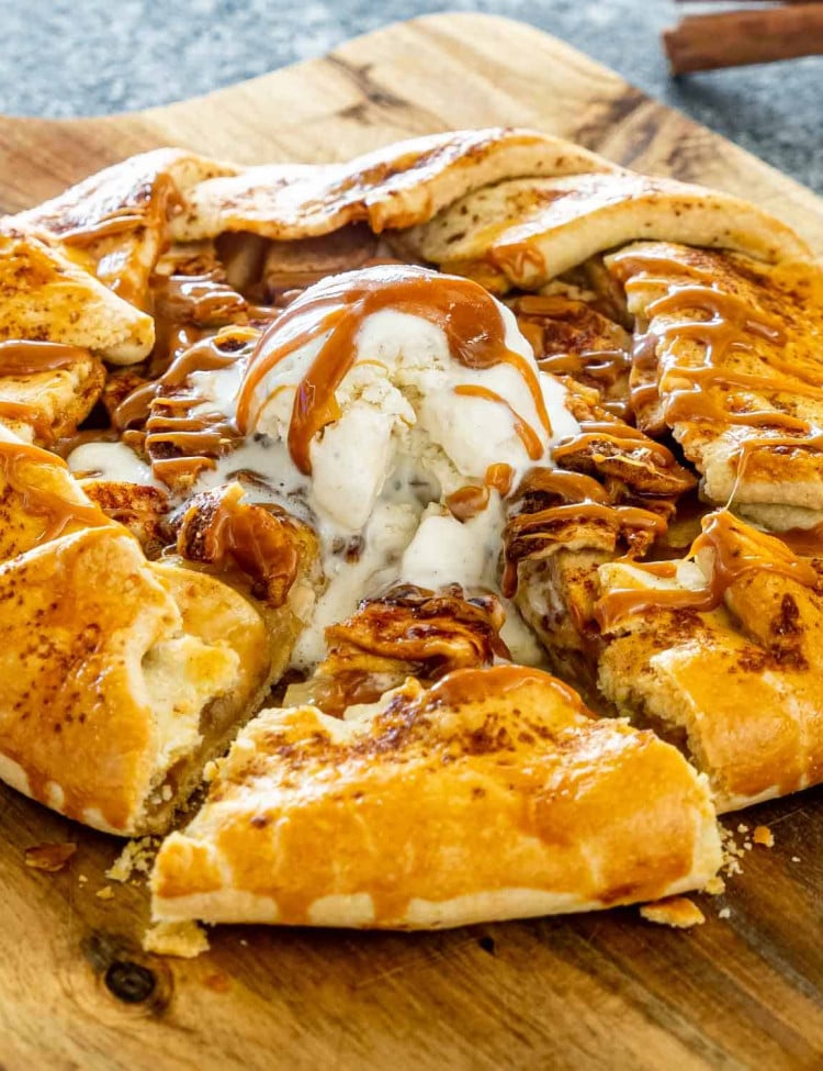 an apple galette with a scoop of ice cream and caramel topping with a slice cut out.