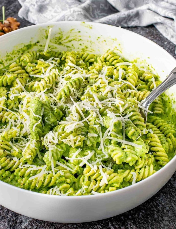 freshly made arugula walnut pesto pasta with parmesan cheese in a white bowl.