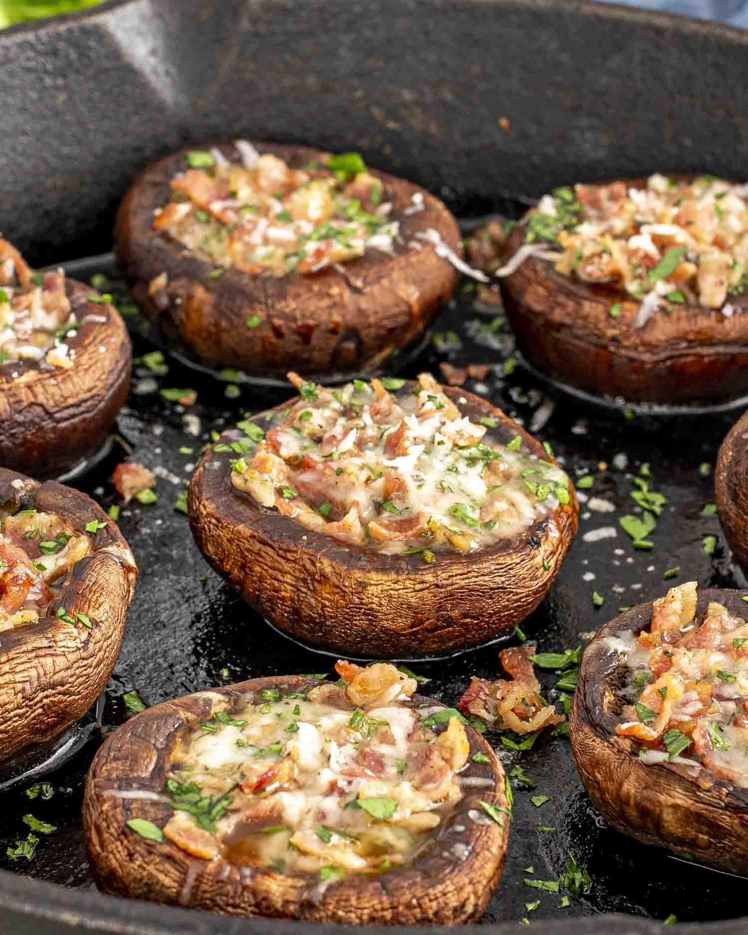 A cast iron skillet filled with freshly baked Bacon Stuffed Mushrooms. The cremini mushrooms are browned and topped with a savory mixture of crispy bacon, melted Parmesan cheese, and fresh parsley, creating a mouthwatering appetizer.