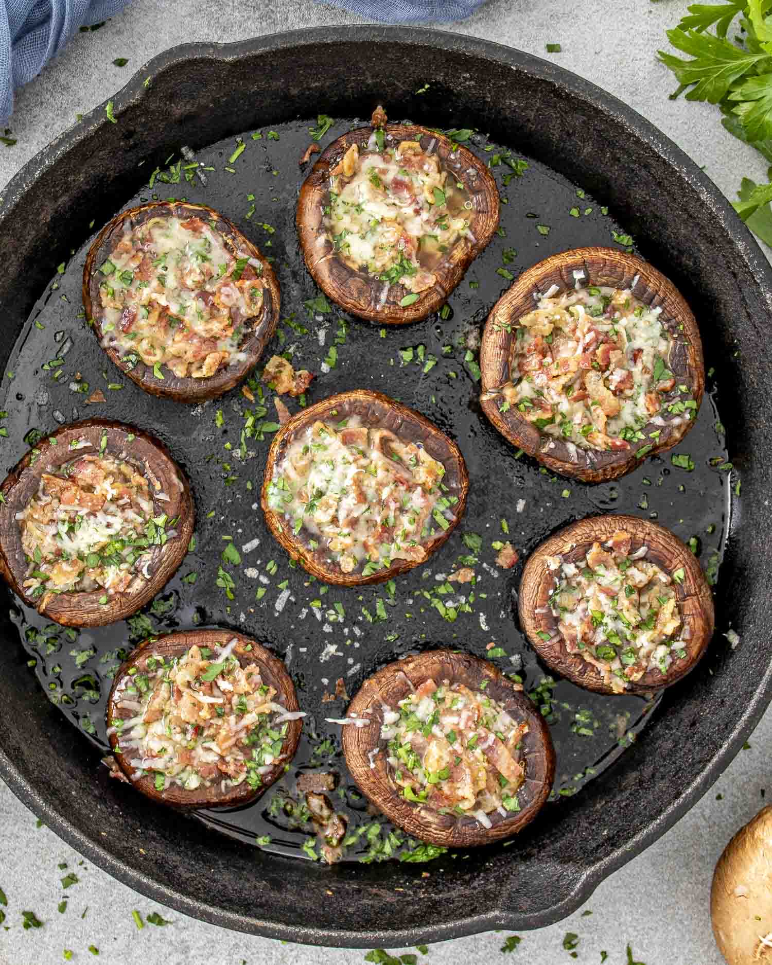 A cast iron skillet filled with freshly baked Bacon Stuffed Mushrooms. The cremini mushrooms are browned and topped with a savory mixture of crispy bacon, melted Parmesan cheese, and fresh parsley, creating a mouthwatering appetizer.