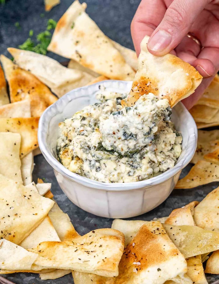 a small bowl with baked feta spinach dip with pita bread for dipping.