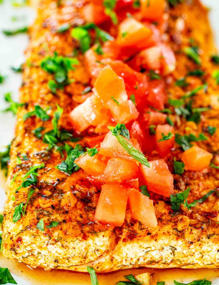 baked lemon garlic halibut filet topped with tomatoes on a white dish.