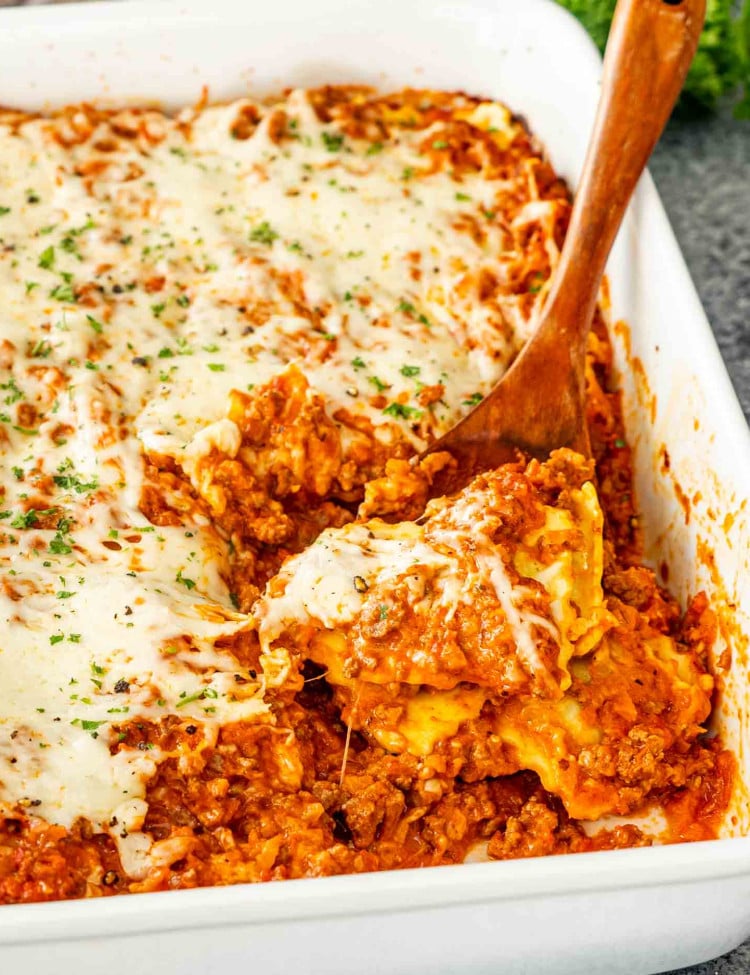 fresh out of the oven baked ravioli in a white casserole dish garnished with a bit of parsley.