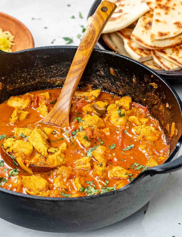 balti chicken garnished with cilantro in a black cast iron pot.