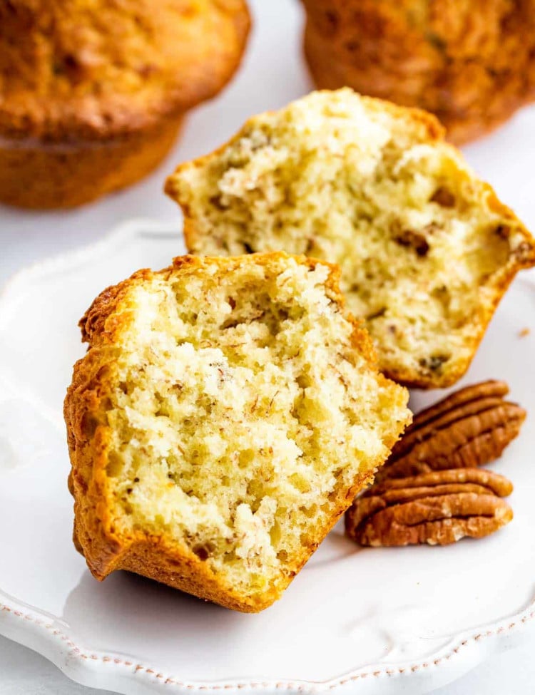 sideview shot of a muffin broken in half on a small white plate with a couple pecan halves on the plate