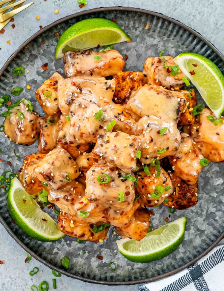 air fryer bang bang salmon on a metal plate garnished with green onions and lime wedges.