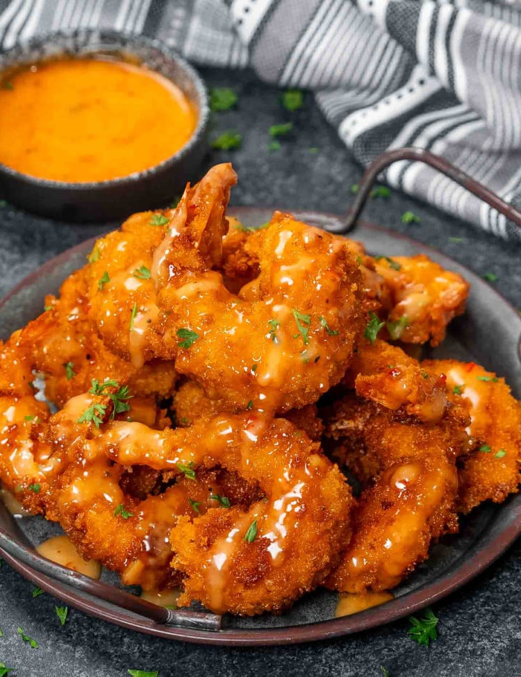 a metal plate filled with bang bang shrimp, crispy and fried and drizzled with a delicious bang bang sauce.