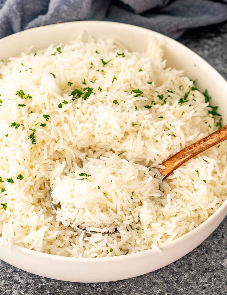 freshly cooked basmati rice in a white bowl garnished with some fresh parsley.