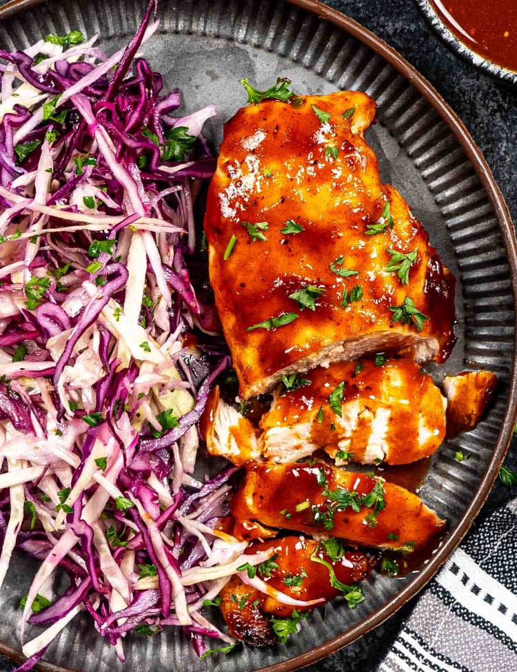 bbq chicken breast with coleslaw on a plate garnished with parsley.