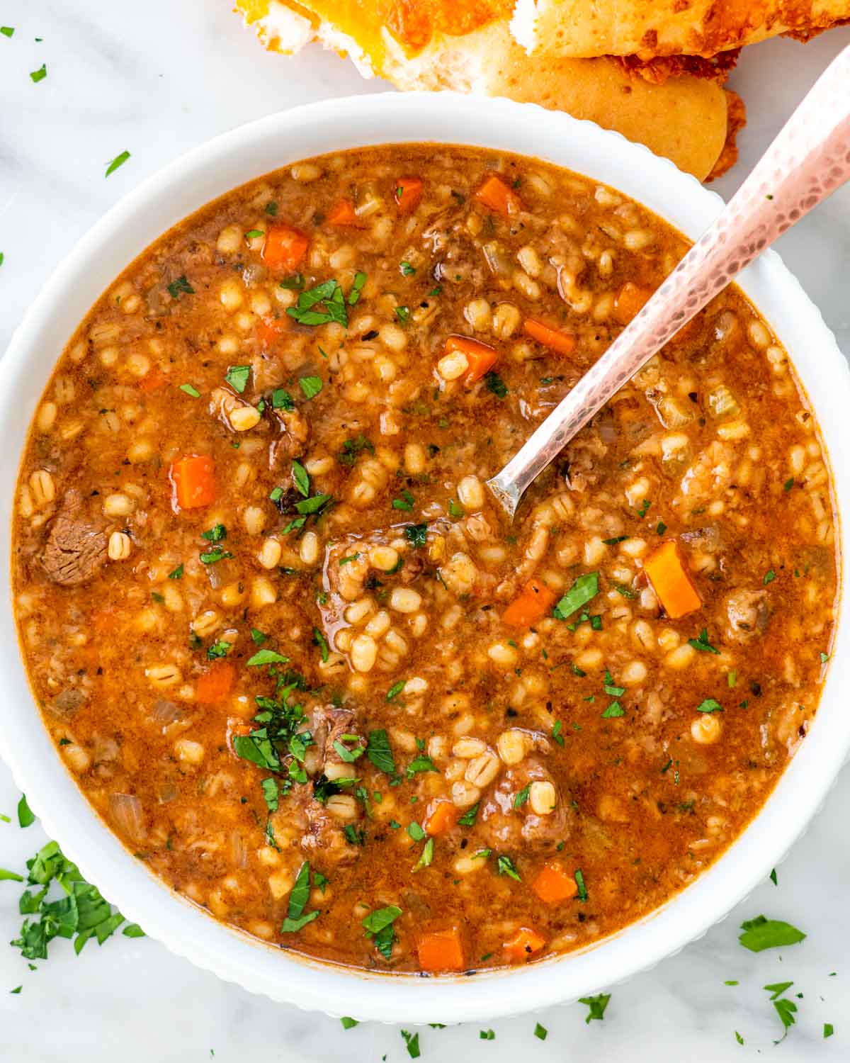 overhead shot of beef barley soup in a white bowl with a spoon inside.