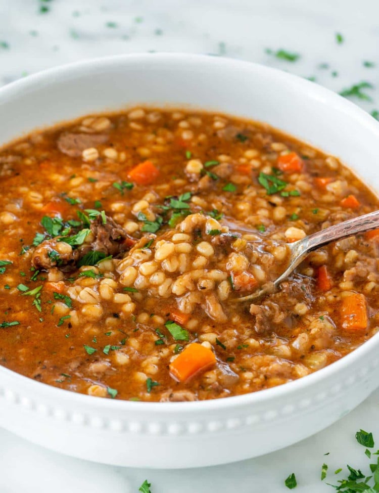 beef barley soup in a white bowl with a spoon inside.