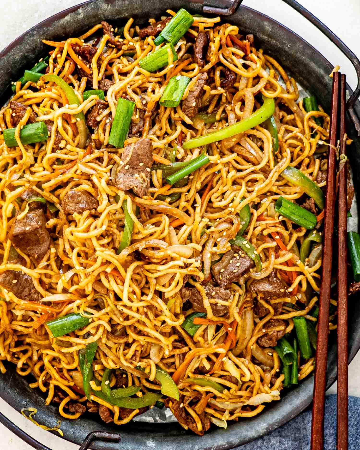 fresh beef chow mein garnished with green onions in a metal plate.