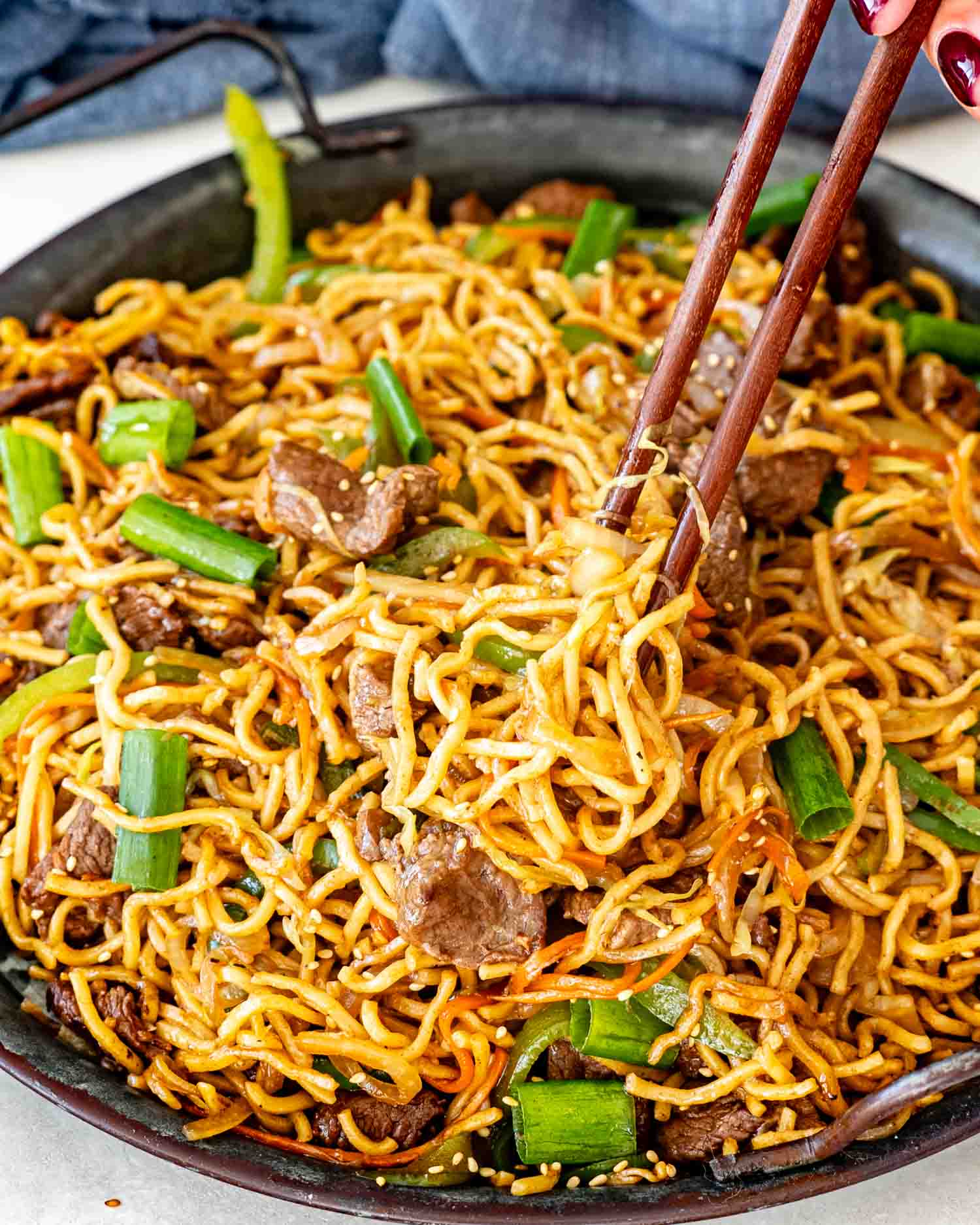 fresh beef chow mein garnished with green onions in a metal plate.