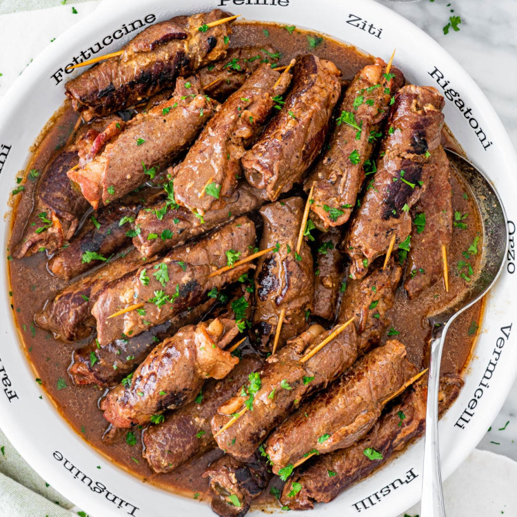 overhead shot of beef rouladen in a large serving bowl with a serving spoon