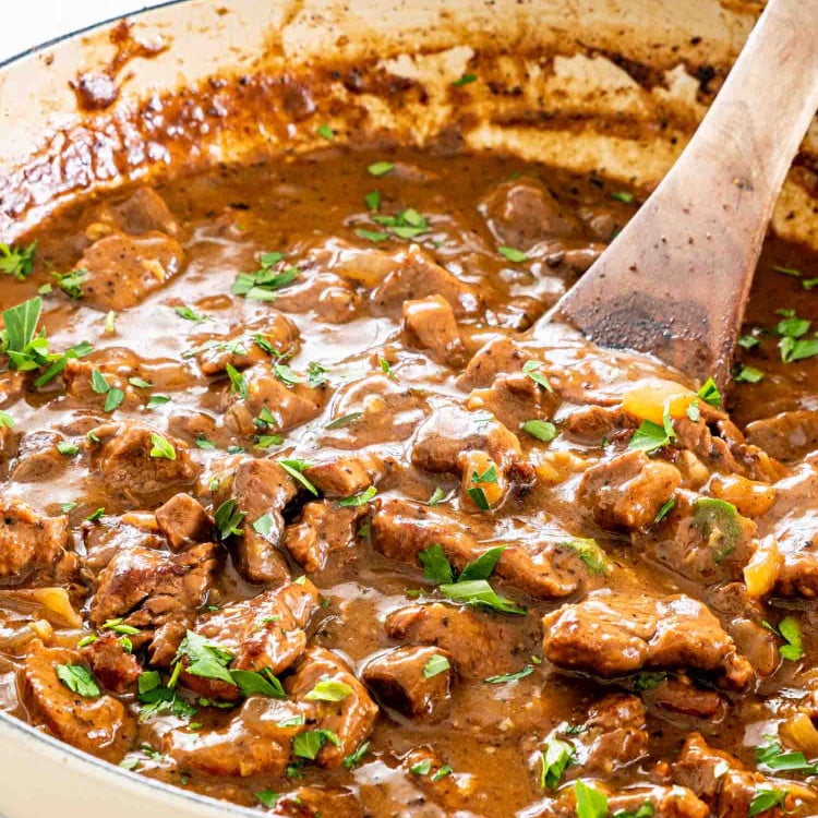 beef tips with gravy in a braiser garnished with parsley.