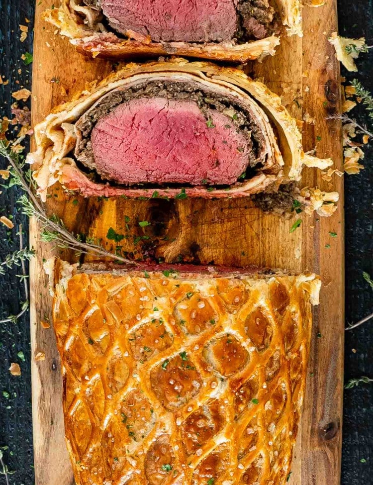 a beef wellington with 2 slices cut on a cutting board.