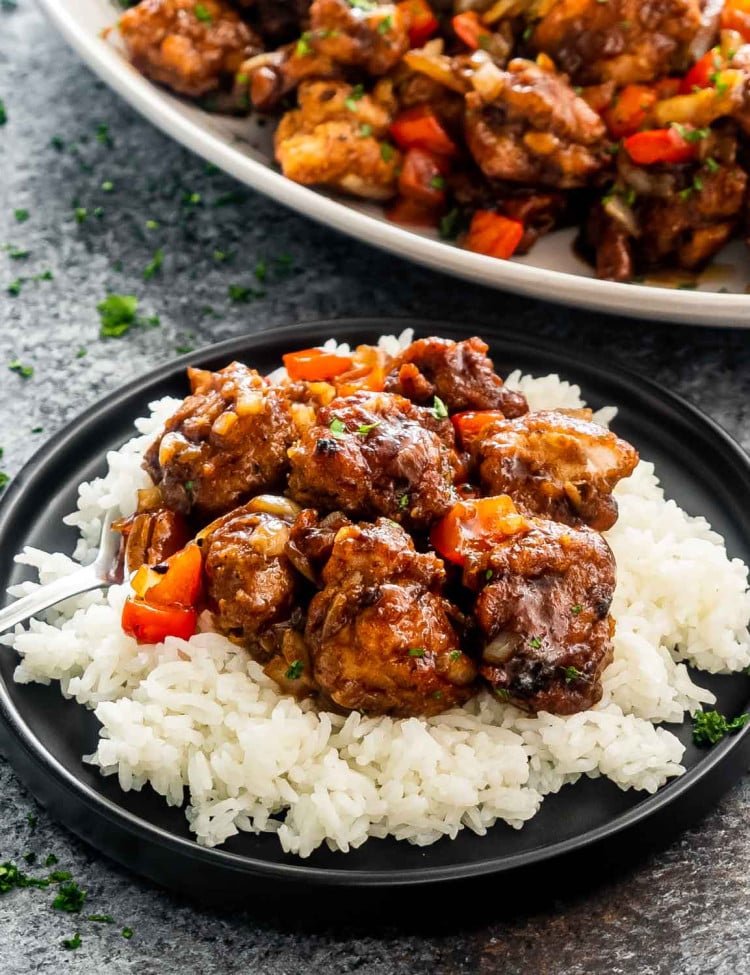 black pepper chicken on a bed of rice on a black plate.