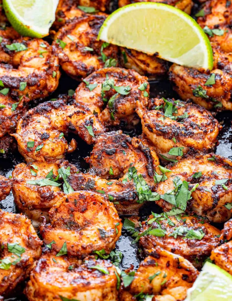 blackened shrimp with lime wedges in a black skillet.