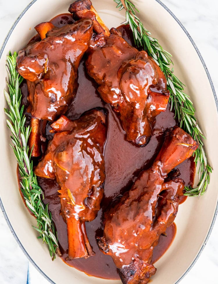 overhead shot of braised lamb shanks in a pot with two sprigs on rosemary