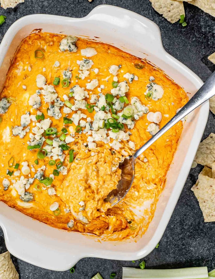 buffalo chicken dip in a square baking dish garnished with blue cheese and green onions.