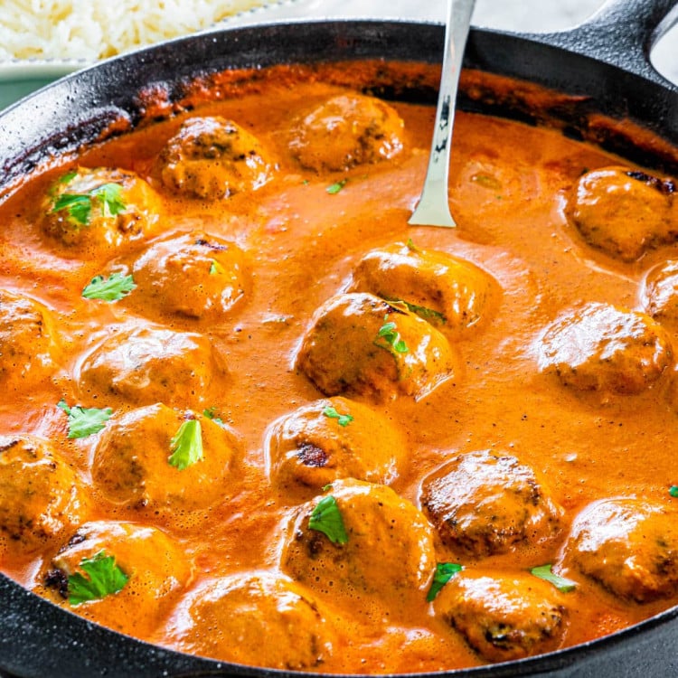 side shot of butter chicken meatballs in a black skillet with a serving spoon inside