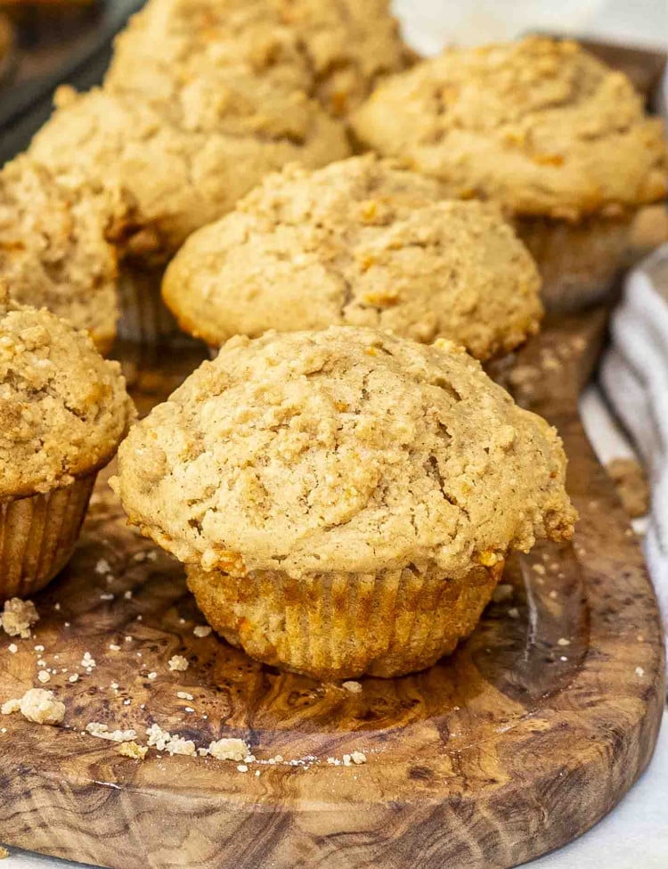 Golden-brown carrot cake muffins with a crumbly, moist texture, nestled in paper liners on a rustic wooden board.