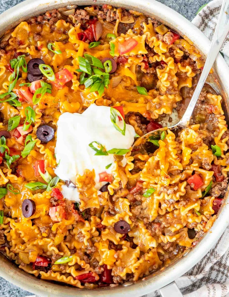 cheesy taco pasta freshly made topped with green onions, tomatoes, olives and a dollop of sour cream.