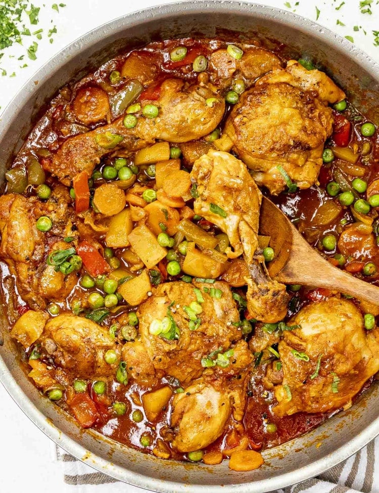 Pan of chicken afritada with tender chicken, potatoes, carrots, peas, and bell peppers in a rich tomato-based sauce.