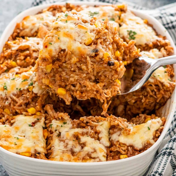 a spatula lifting a piece of chicken enchilada rice casserole from a casserole dish.