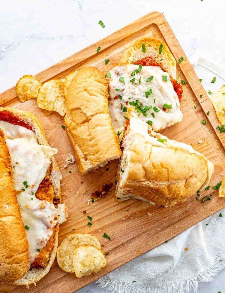 2 chicken parmesan subs on a rustic cutting board garnished with parsley.