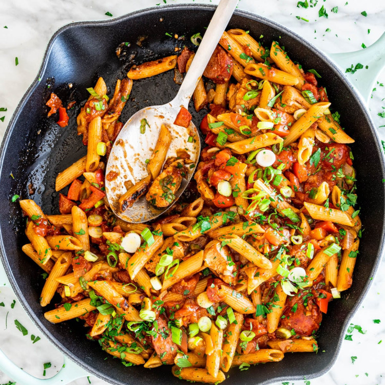 overhead shot of chicken jambalaya penne in a skillet with a serving spoon in it