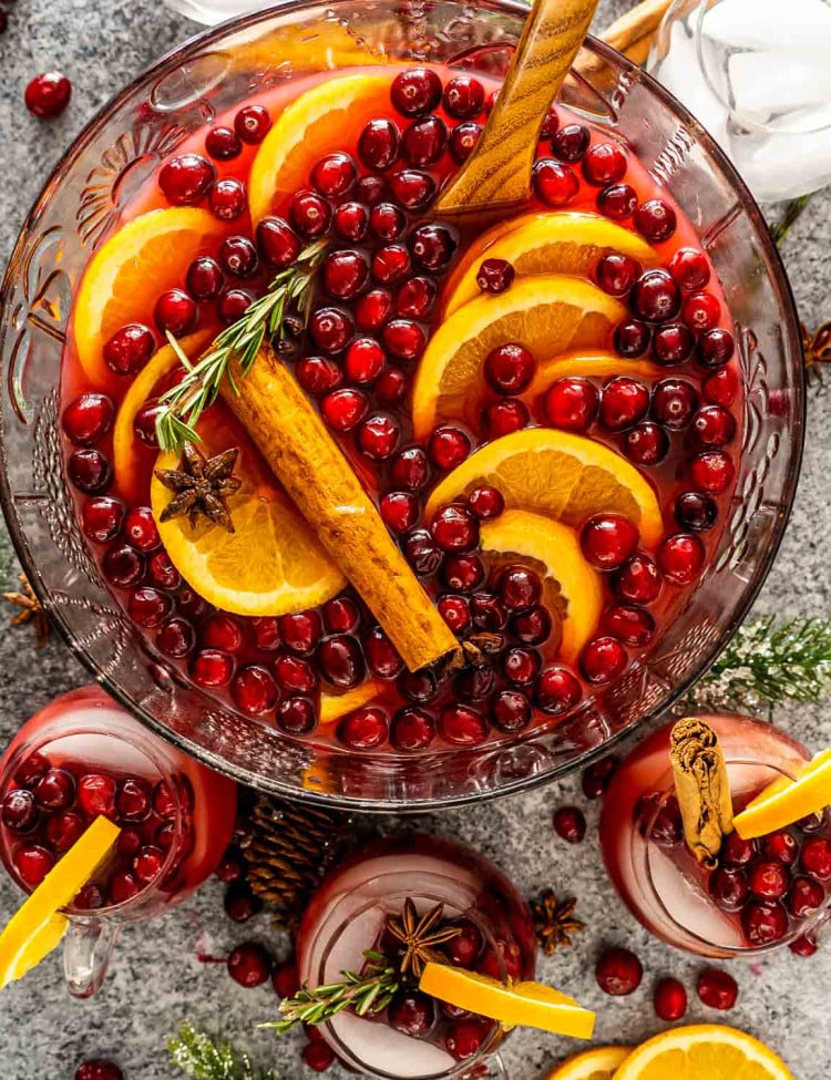 christmas punch in a punch bowl with a few cups filled with punch around it.