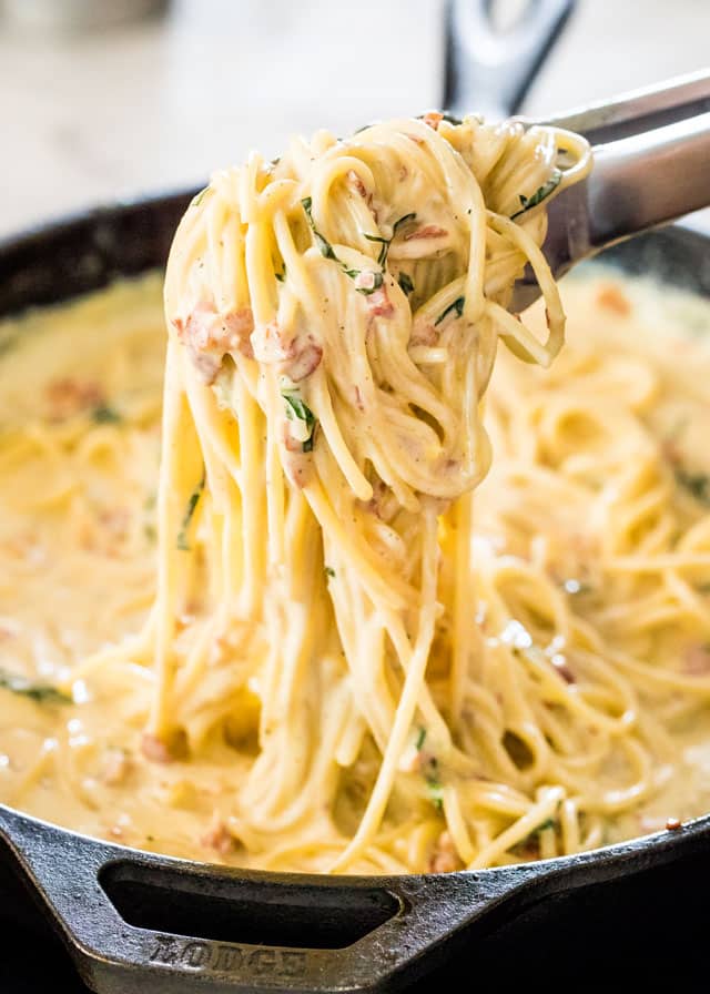 side view shot of tongs holding up some creamy carbonara