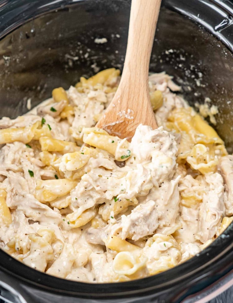 chicken alfredo in a crockpot with a wooden spoon inside.