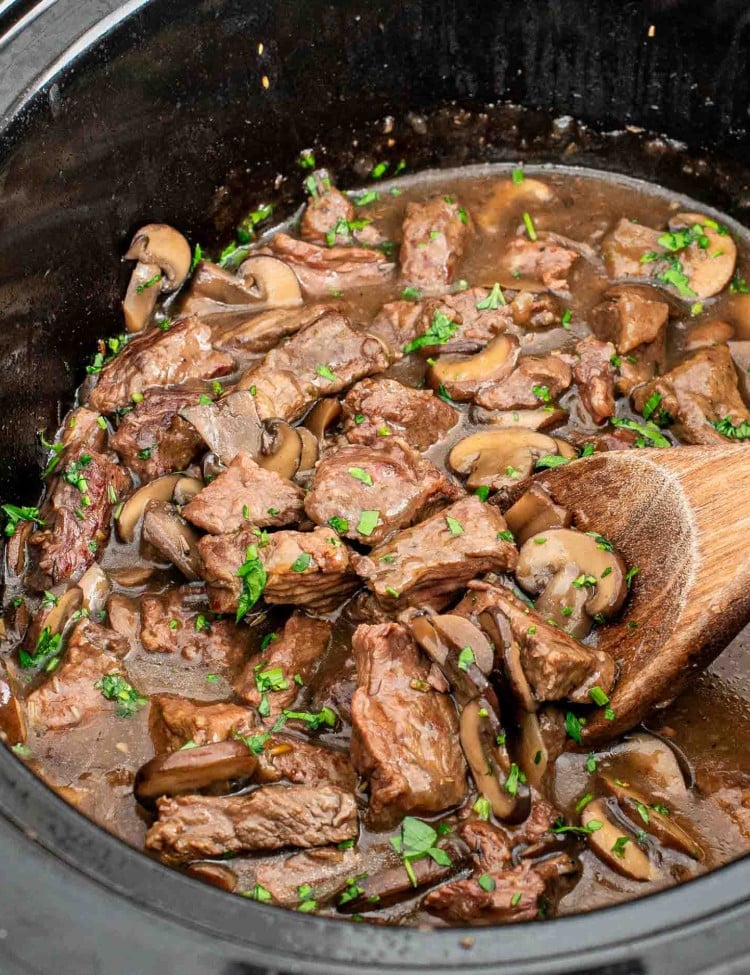 a crockpot with steak and gravy garnished with parsley.