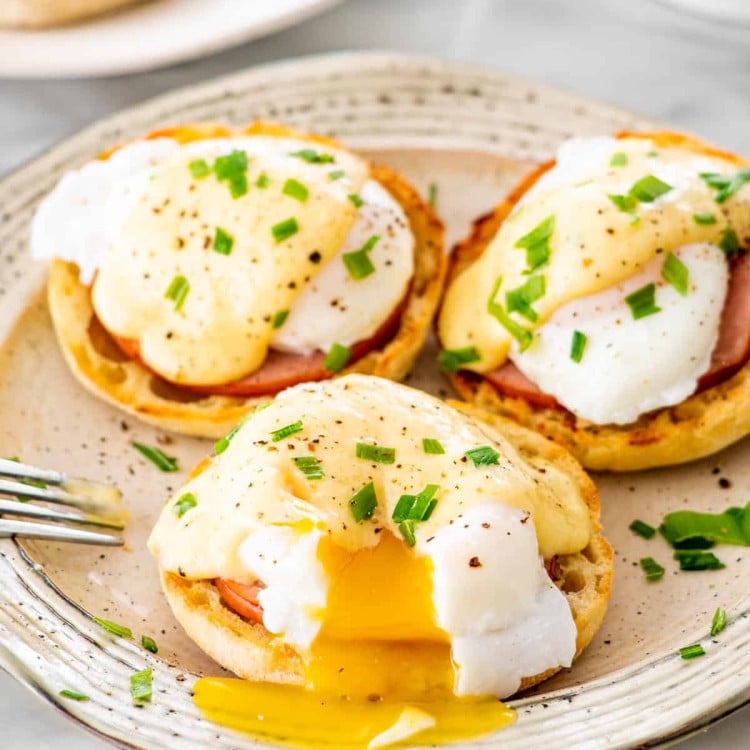 3 eggs benedict on a large plate garnished with chives