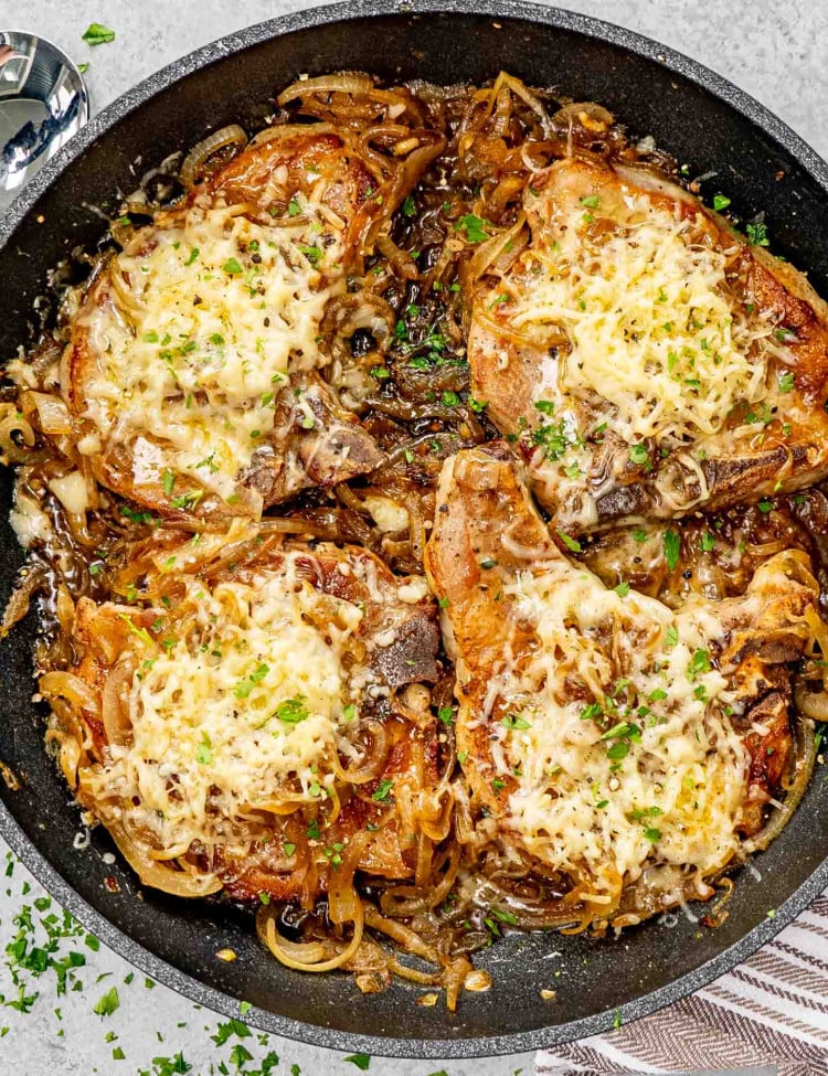 French onion pork chops in a skillet garnished with fresh thyme and parsley.