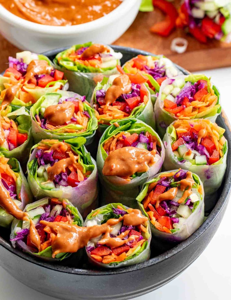 spring rolls cut in half in a black bowl with peanut sauce.