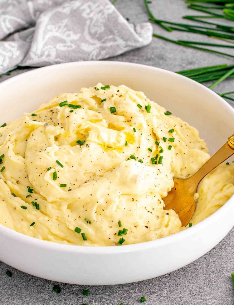 a white bowl with garlic mashed potatoes and a pat of butter on top and garnished with chives.