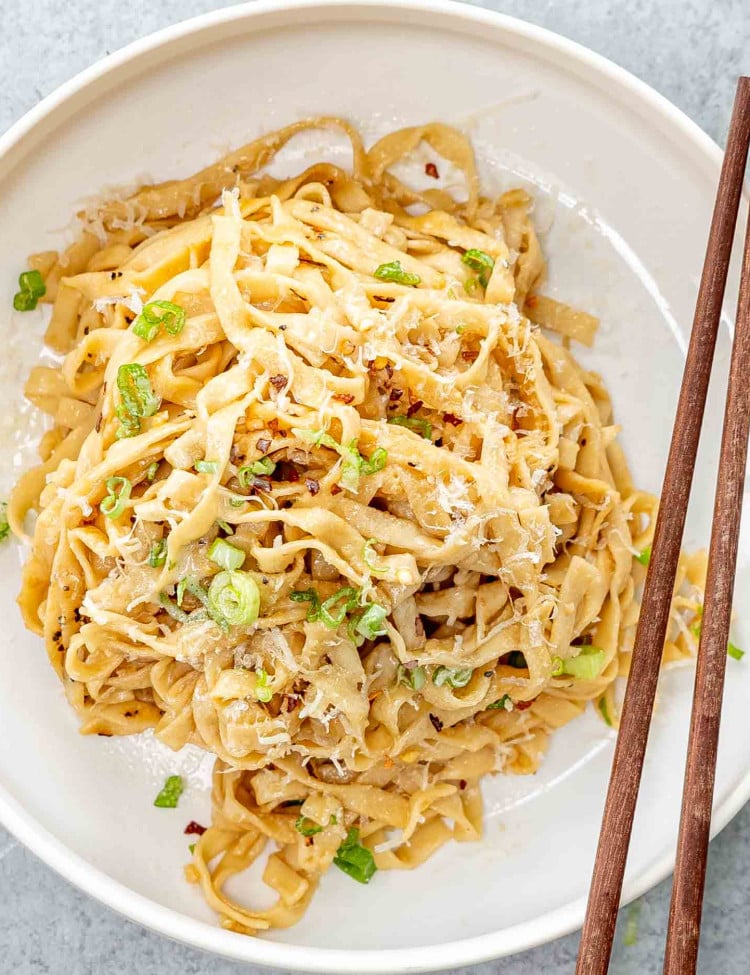 a serving of garlic noodles in a white bowl garnished with green onions.