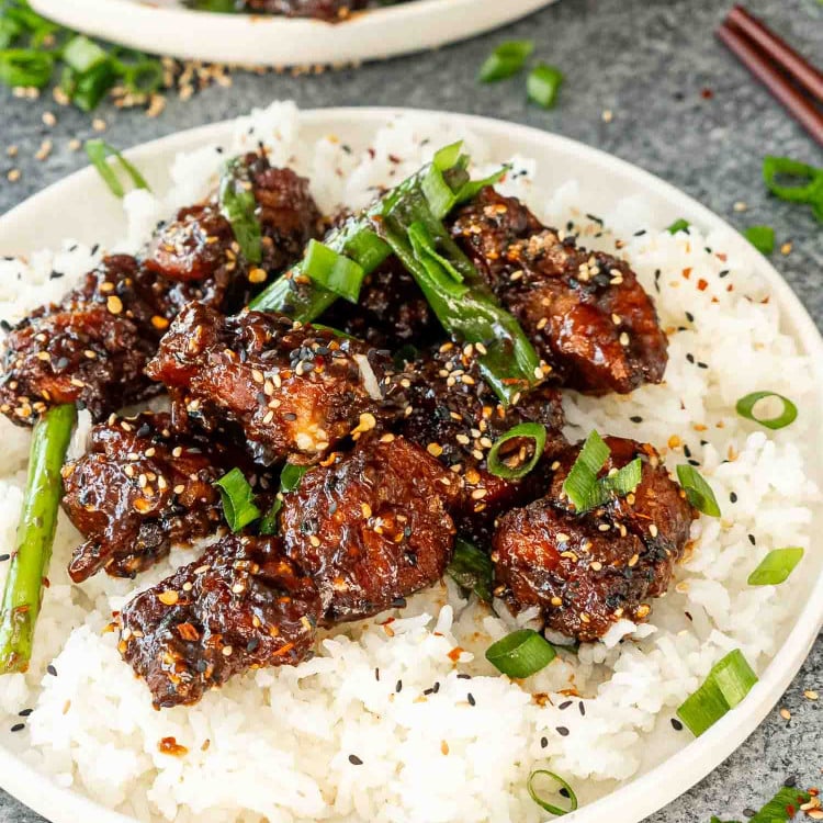 freshly made general tso's chicken garnished with green onions and sesame seeds over a rice in a white plate.