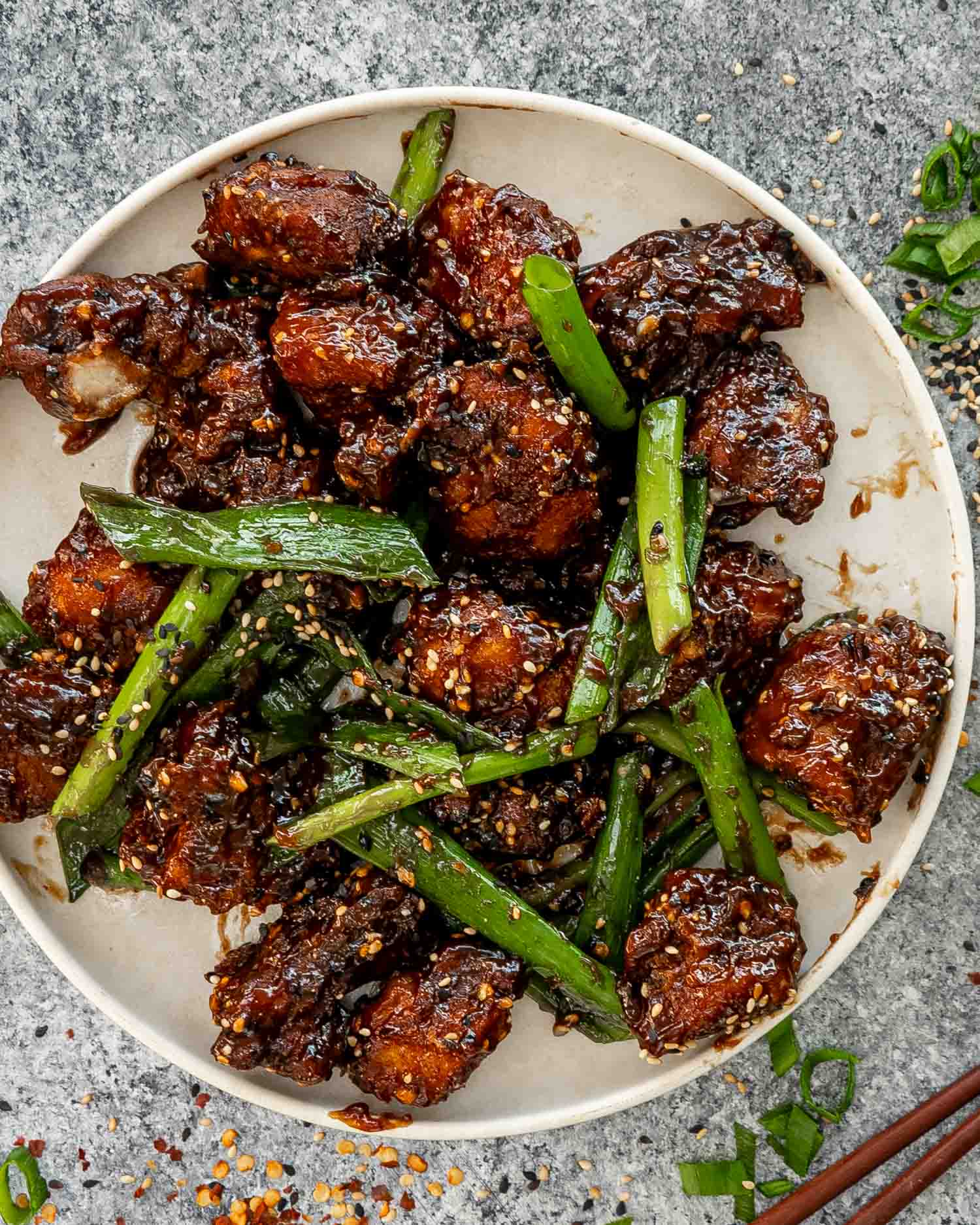 freshly made general tso's chicken garnished with green onions and sesame seeds in a white plate.