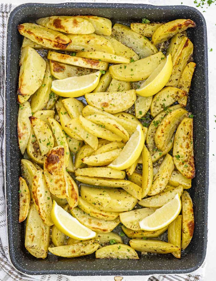 fresh out of the oven greek potatoes garnished with parsley in a baking dish.