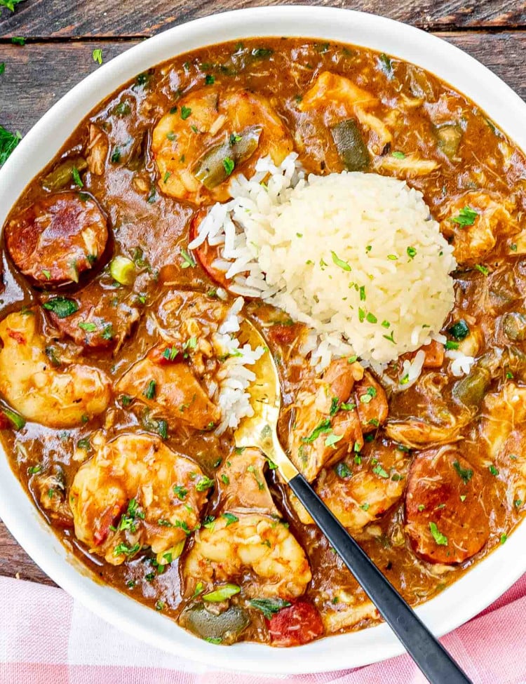 freshly made gumbo in a white bowl with a scoop of rice and garnished with some parsley.