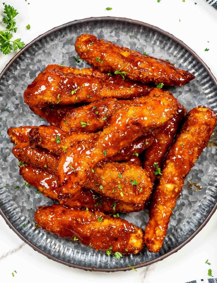 air fried honey bbq chicken tenders on a metal plate garnished with parsley.