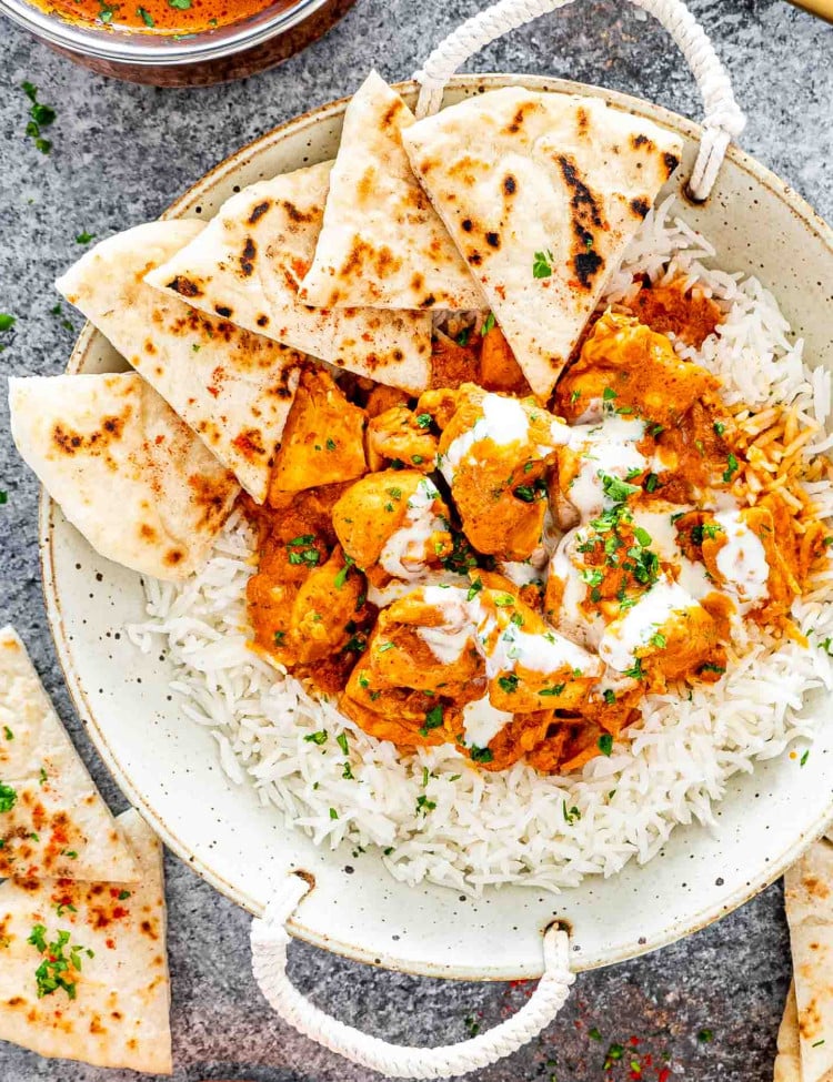 butter chicken over a bed of rice on a plate with naan.