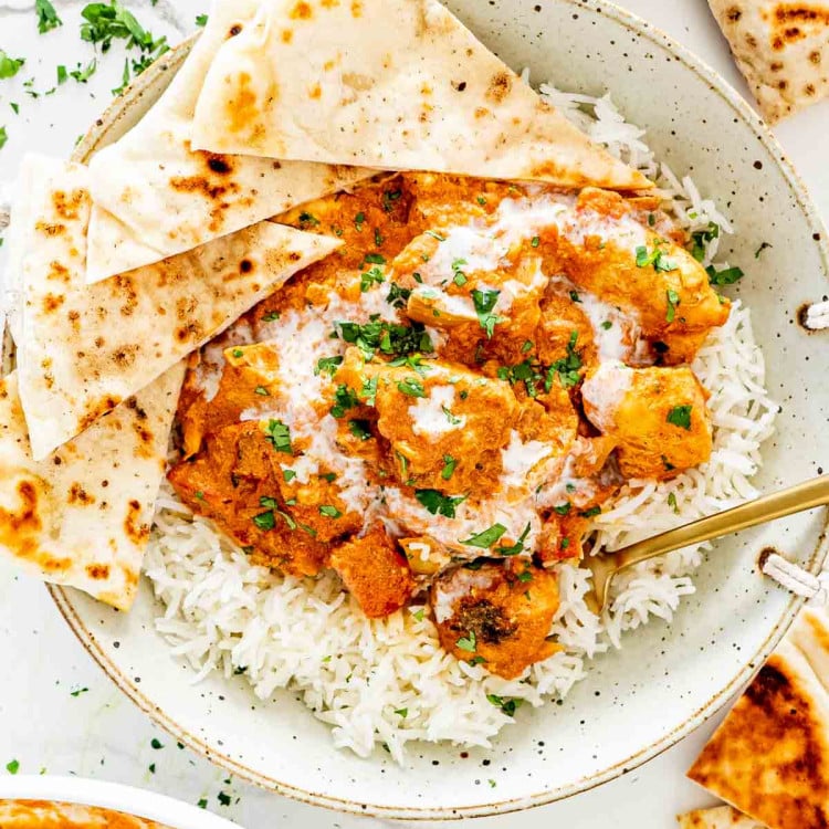 chicken tikka masala in a plate with rice and garnished with cilantro.