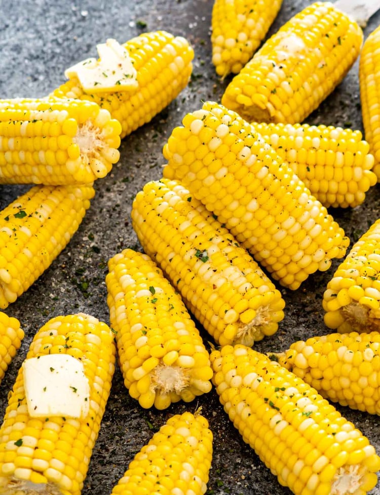 a few corn on a table some with a pat of butter.