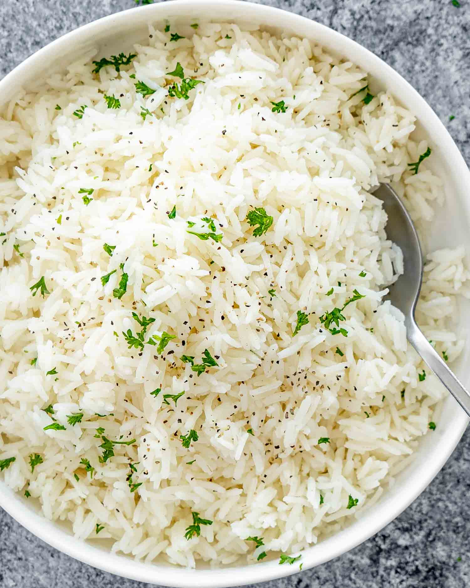 a white bowl with perfectly cooked jasmine rice garnished with some parsley.